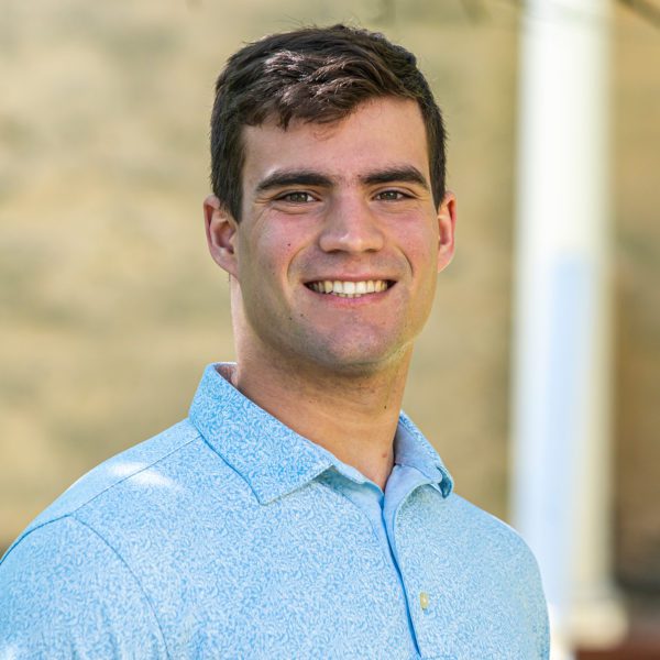 Nathaniel Ruhl stands in front of a wall, smiling.