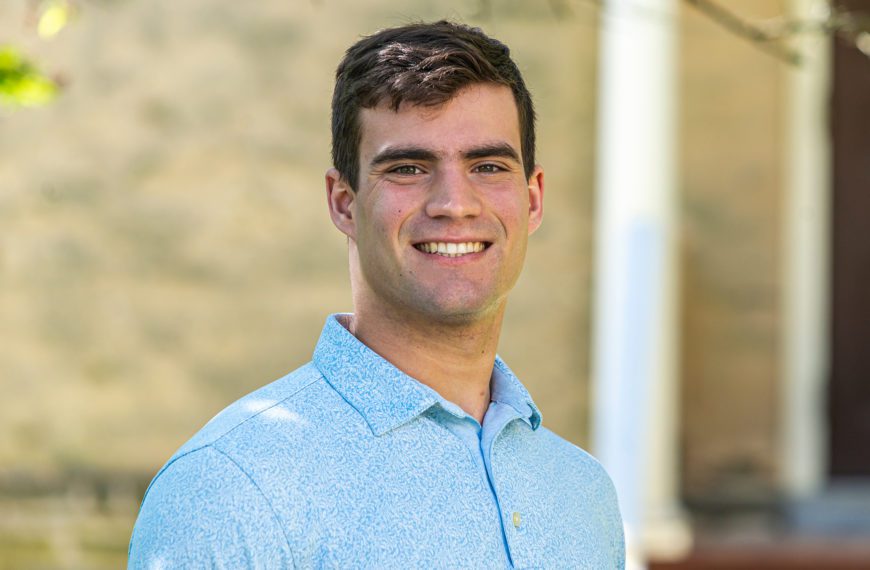 Nathaniel Ruhl stands in front of a wall, smiling.