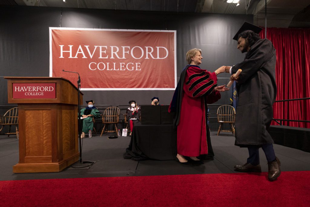 A student smiles and fist bumps President Raymond as she hands off the diploma.