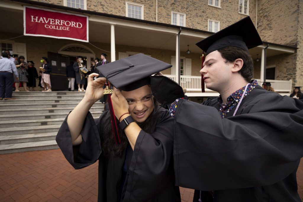 A student helps a friend with her cap in front of Founders Hall.