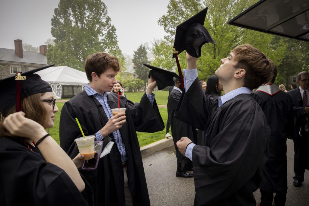 Three members of the Class of 2022 adjust their caps and drink smoothies.