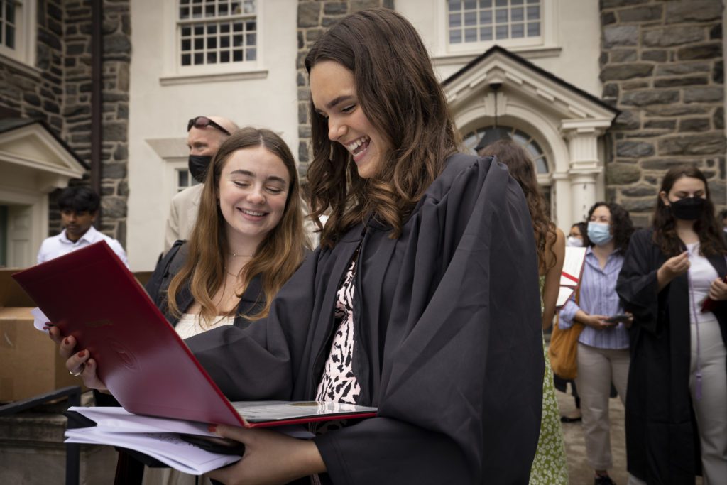 Two students look at their diplomas in their red cases and smile.
