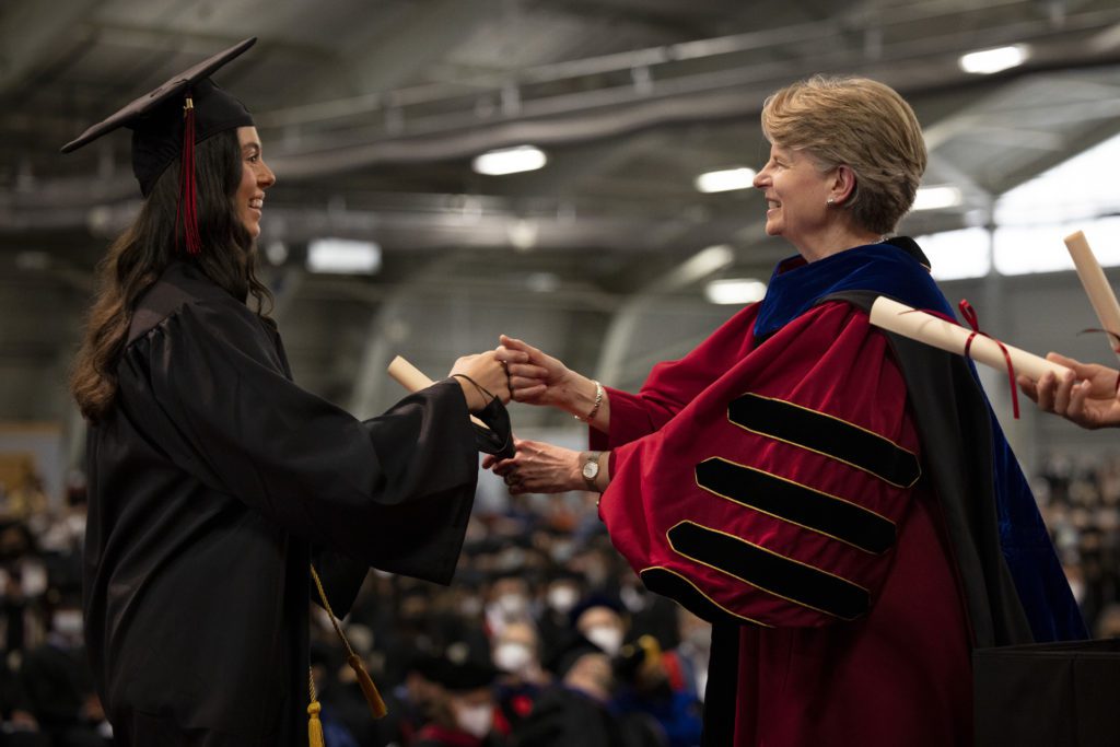 President Raymond and a student smile and fist bump during the diploma exchange.
