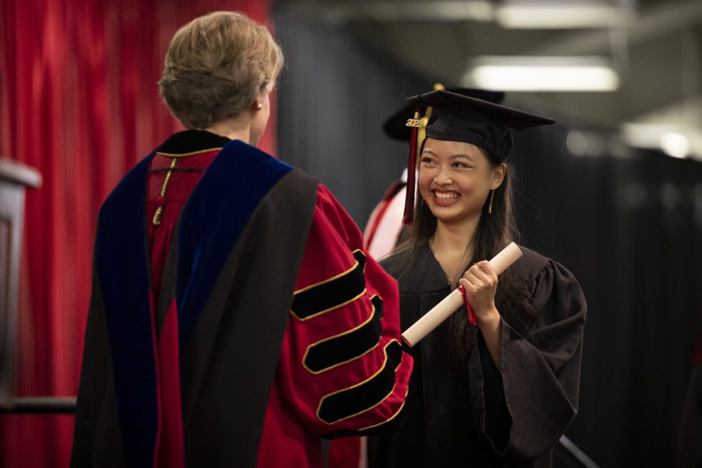 A student smiles as she takes her diploma from President Raymond.