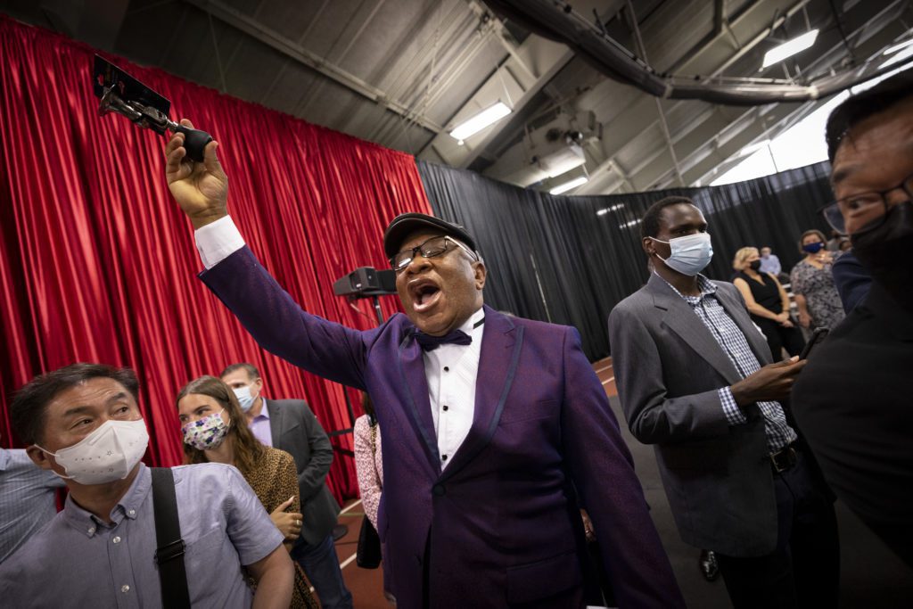 A family member of a graduate, in a purple tuxedo, cheers and squeezes a horn in the air.