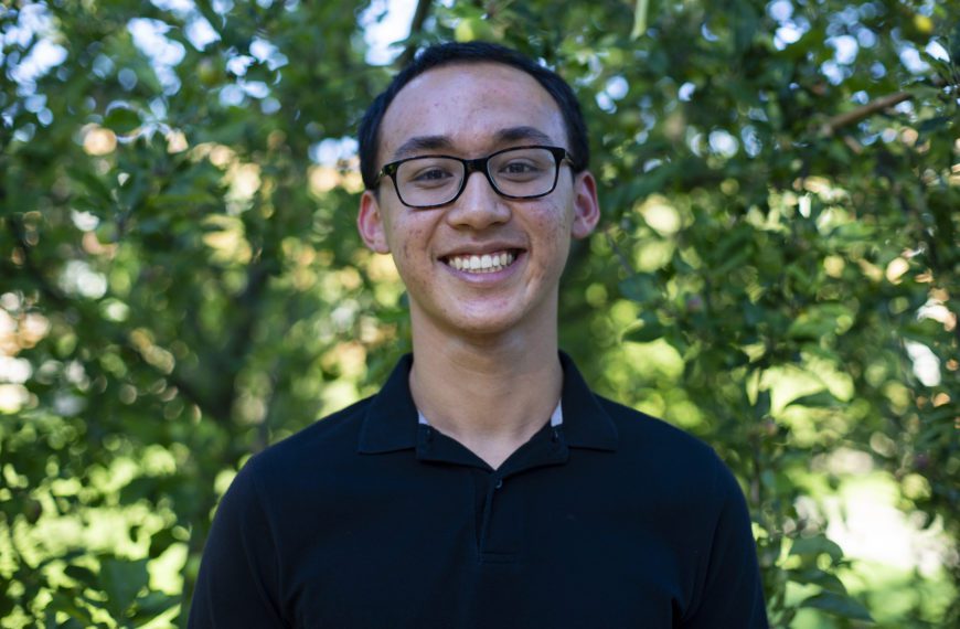 Theo smiles to the camera with trees in the background