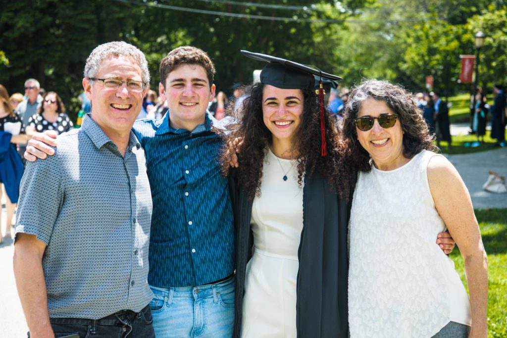 A member of the Class of 2020 wears a white dress under her graduation gown and poses with three members of her happy family.