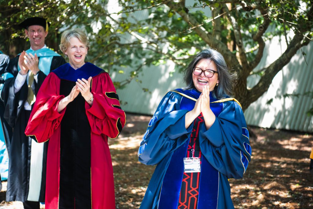 The three administrators wear their academic regalia and smile and clap.