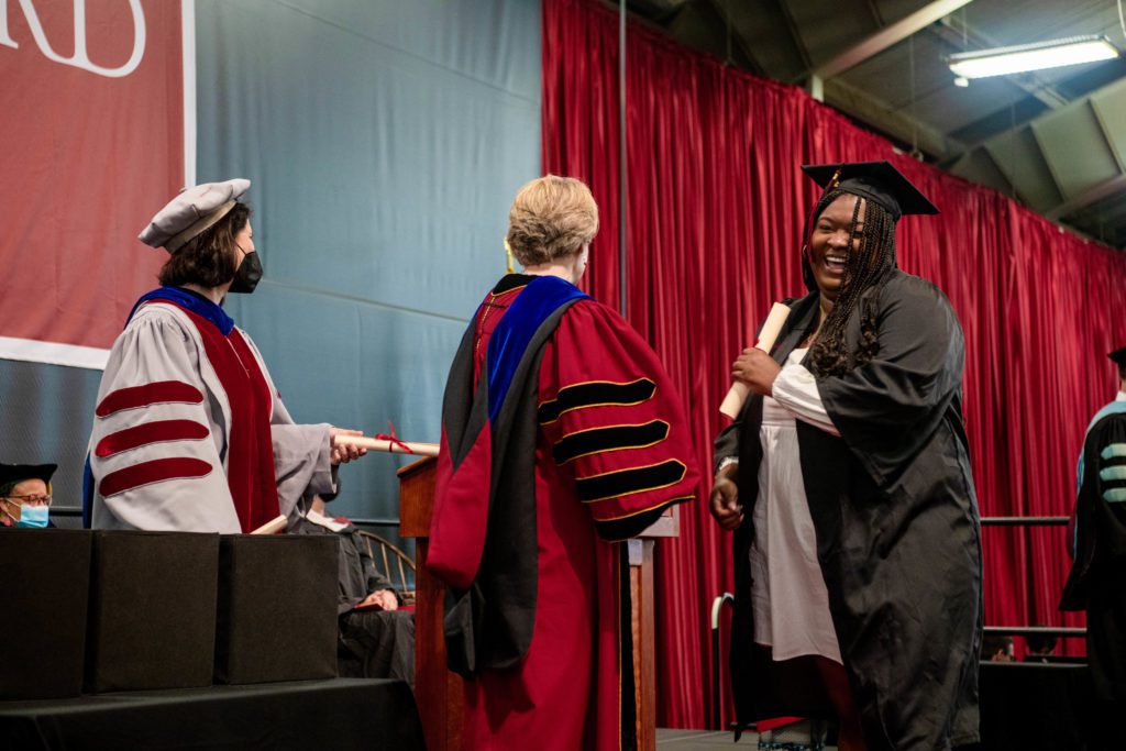 A graduate laughs after taking her diploma from President Raymond onstage