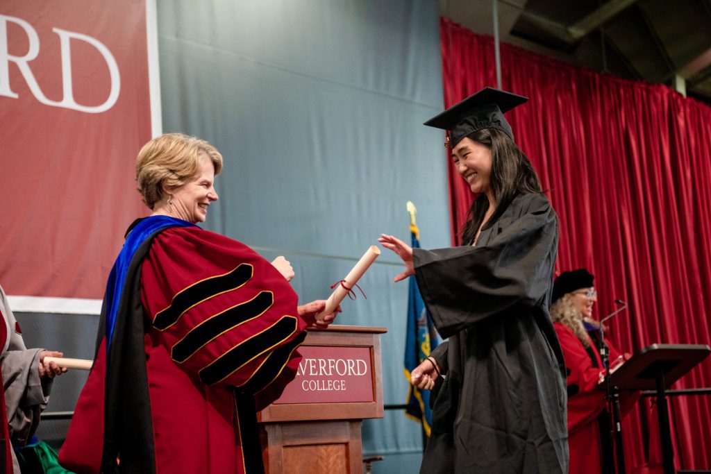 A graduate takes a diploma scroll from the president onstage.