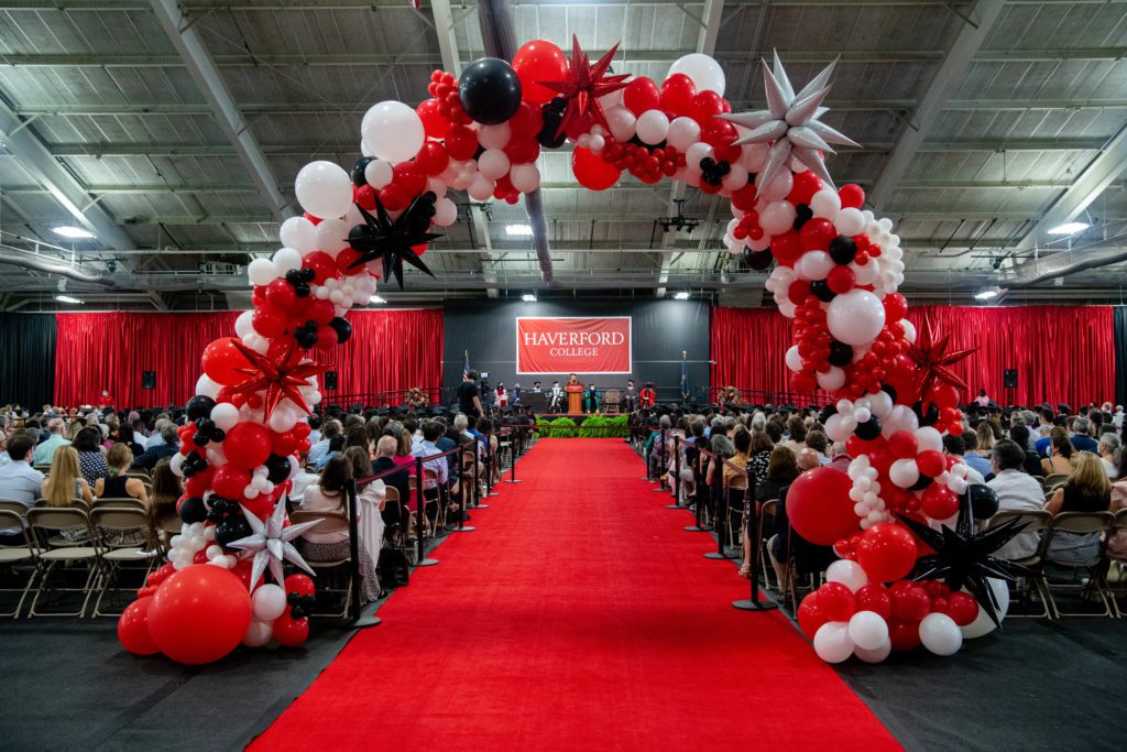 A view of the speakers on stage from the back of the audience through the balloon arch