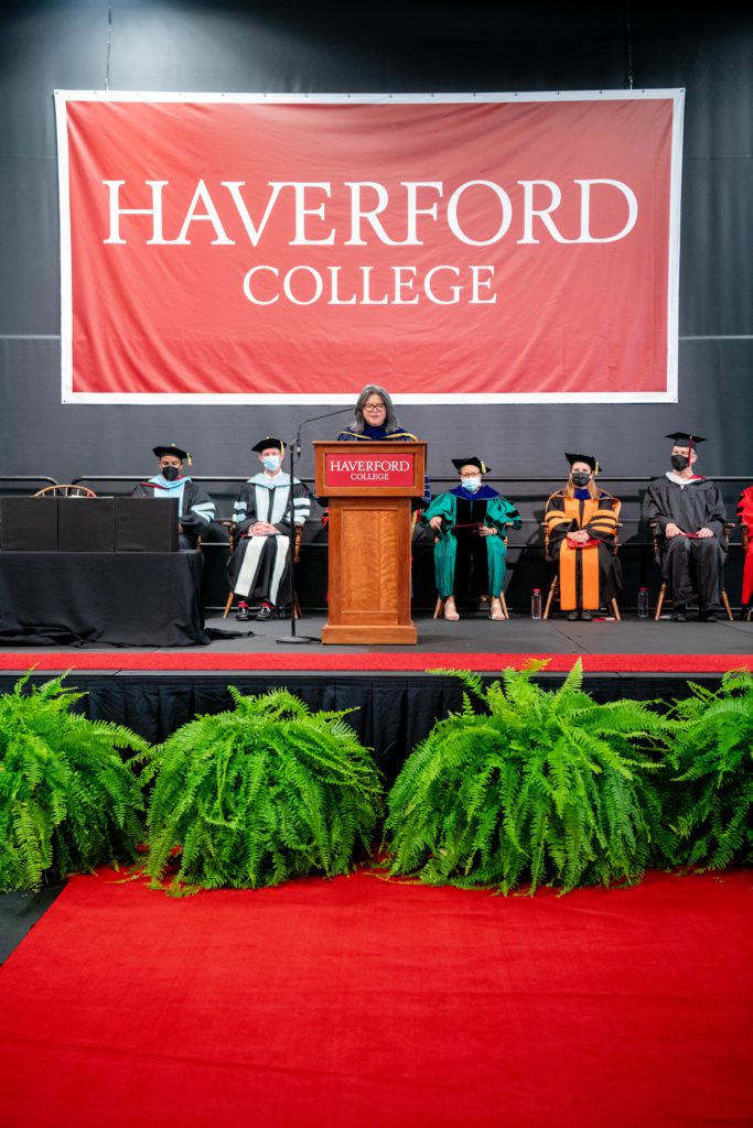Theresa stands at a podium in academic regalia under a giant Haverford College banner.