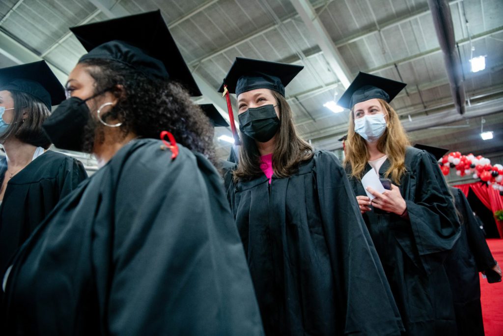 Three graduates walk down the red carpet in their masks and graduation caps and gowns.