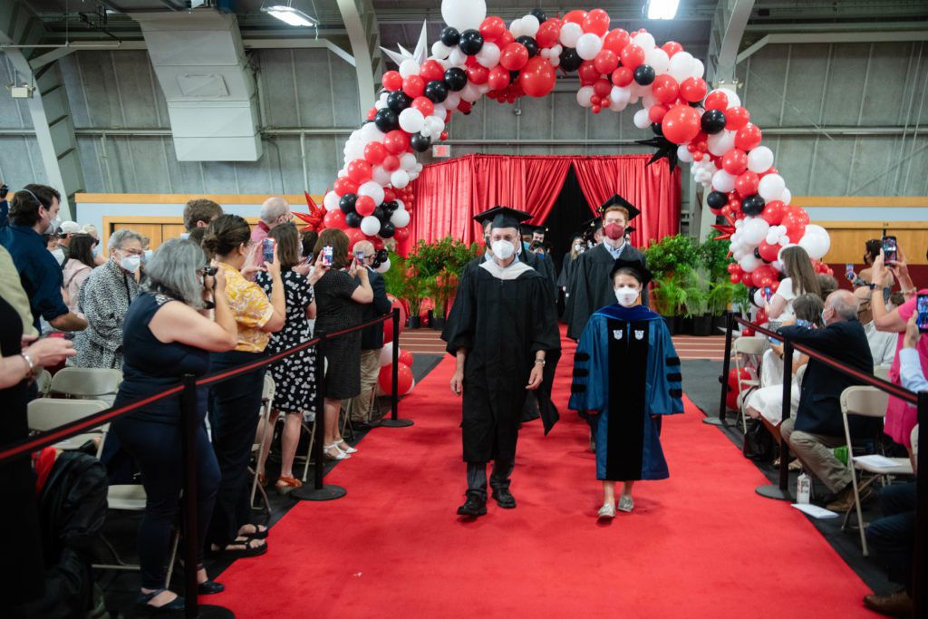 The first faculty members in the processional enter through a balloon archway as guests turn to take their photos.