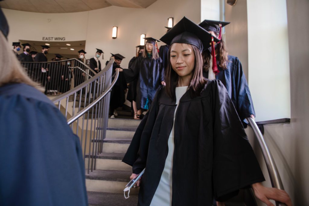 A line of black-clad graduates process down the stairs in the KINSC to the Field House