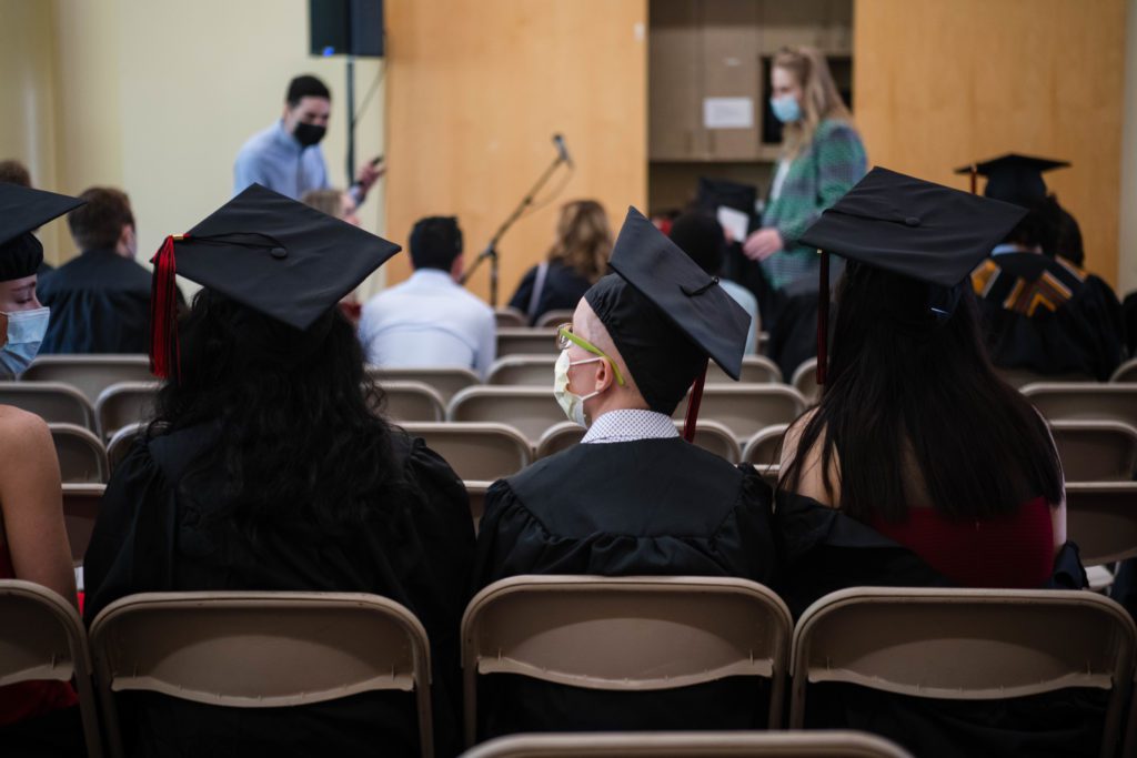 Three seated graduates in their caps and gowns photographed from behind.