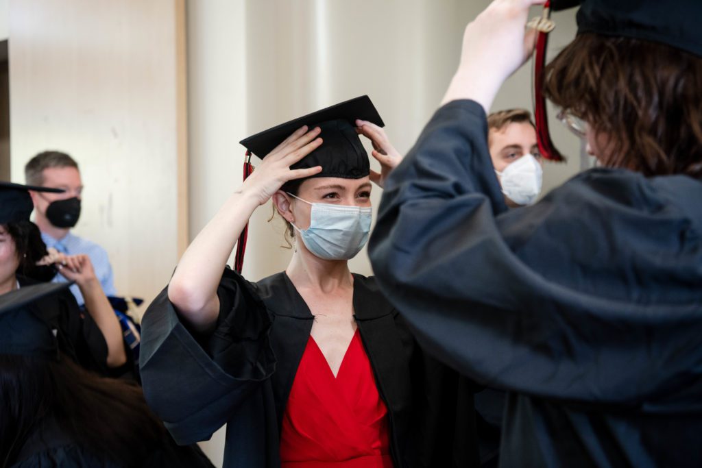 A masked graduate adjusts her cap