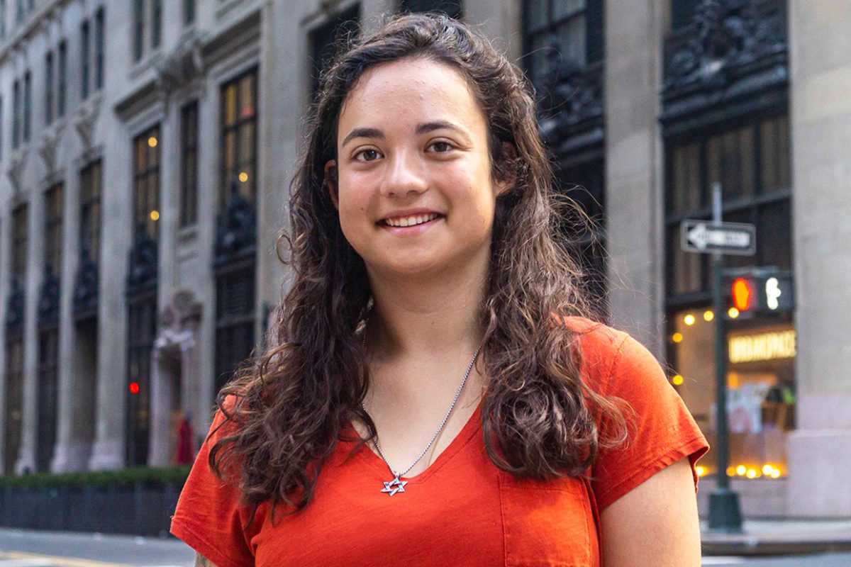 Anne wears an orange shirt and smiles on a Manhattan street