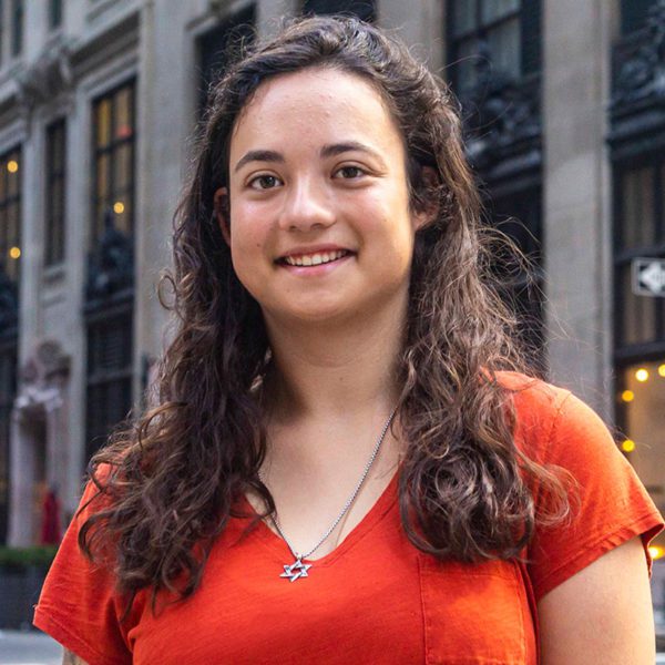 Anne wears an orange shirt and smiles on a Manhattan street