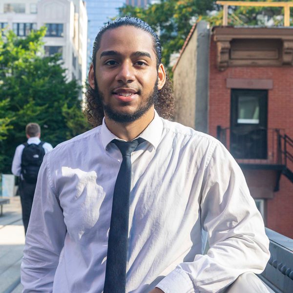 Ivan smiles, wearing a tie, in the street in Lower Manhattan