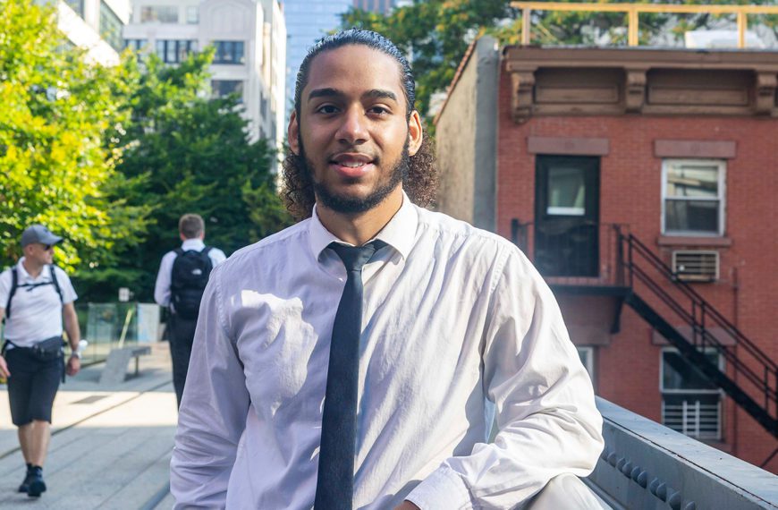 Ivan smiles, wearing a tie, in the street in Lower Manhattan