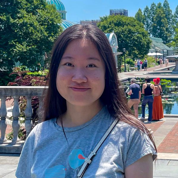 Ziyao Wang '22 stands outside in front of a pavilion of fountains and trees.