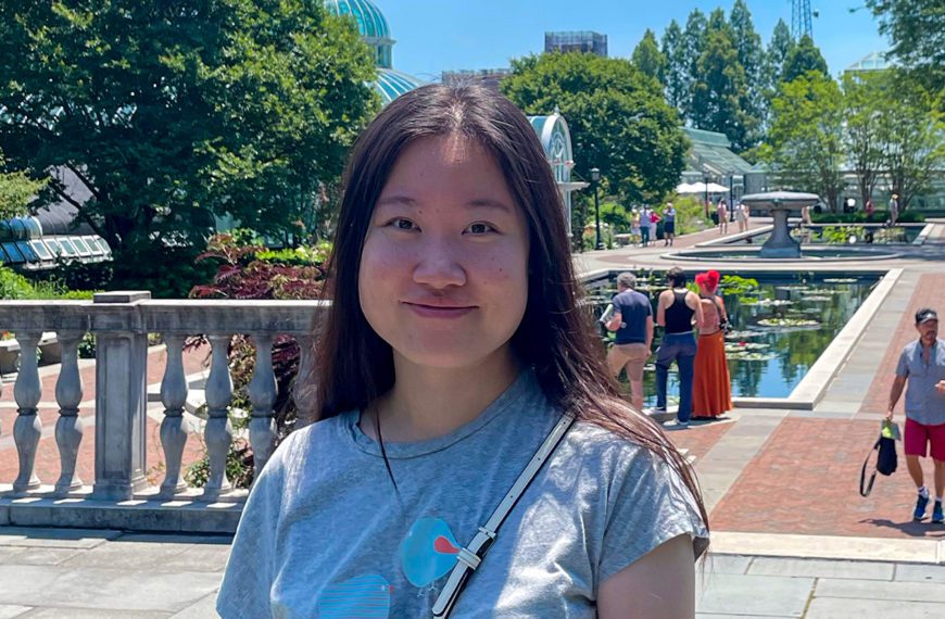 Ziyao Wang '22 stands outside in front of a pavilion of fountains and trees.