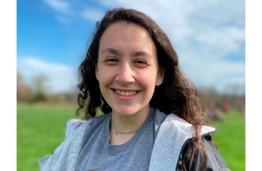 Rebecca smiles for the camera, green field in the background