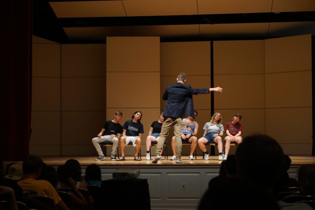 Six people with their eyes close sway to the right as the hypnotist reaches out his right arm.