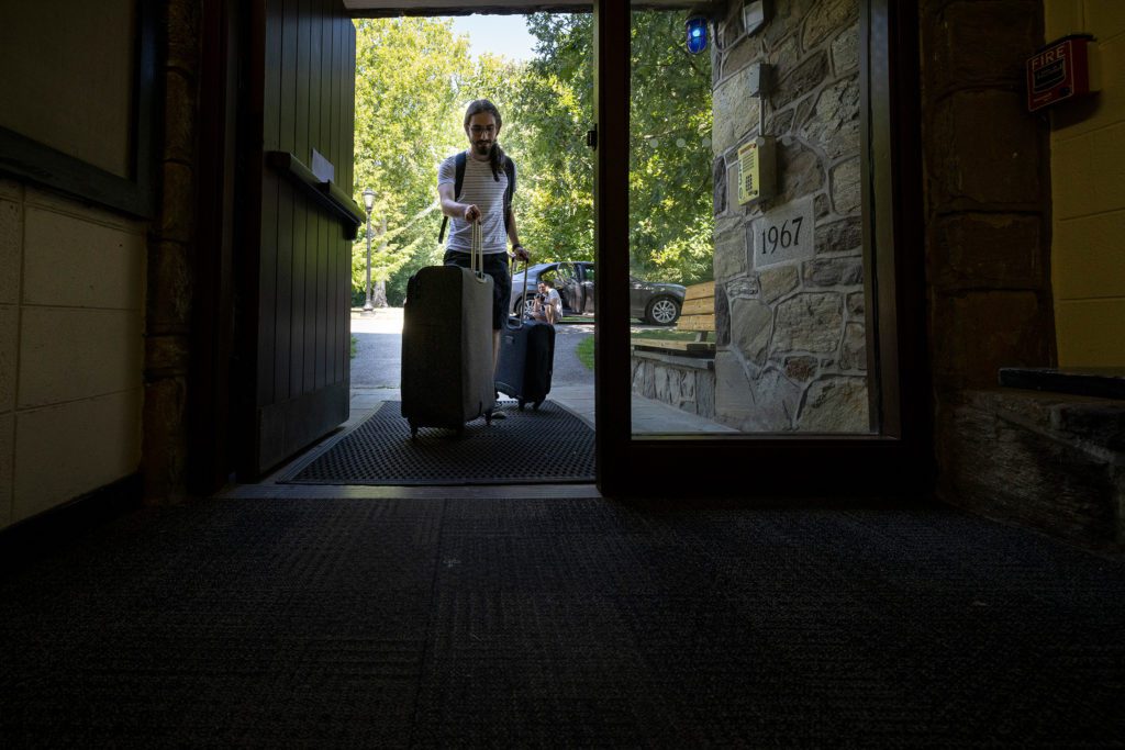 A student wheels two suitcases into a door from a car parked outside.