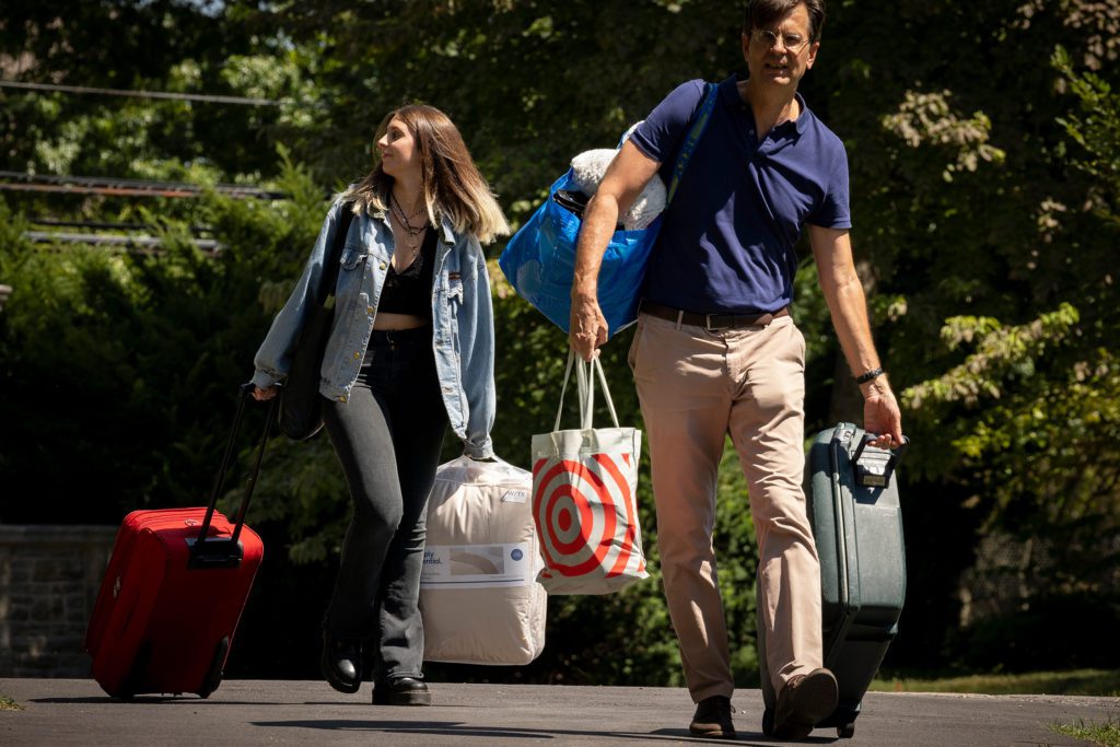 A father and his student wheel suitcases and carry bags to her dorm.