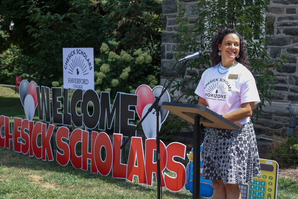 Christina Rose wearing a Chesick Scholar Horizons t-shirt stands in front of a giant lawn sign reading "Welcome Chesick Scholars"