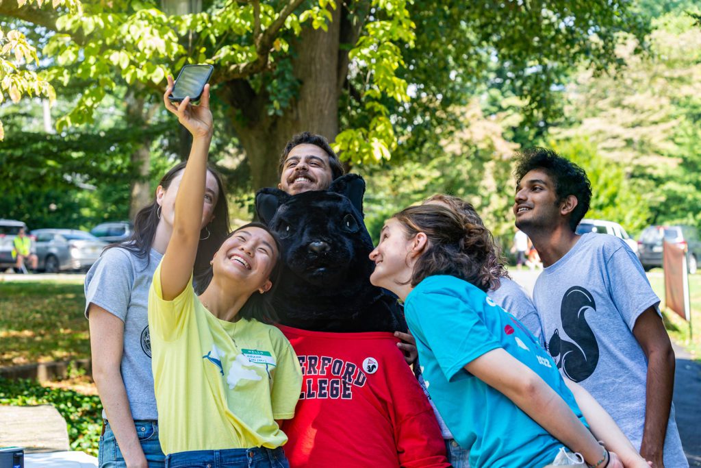 Six students in different Customs tshirts pose around the Black Squirrel mascot for a selfie.