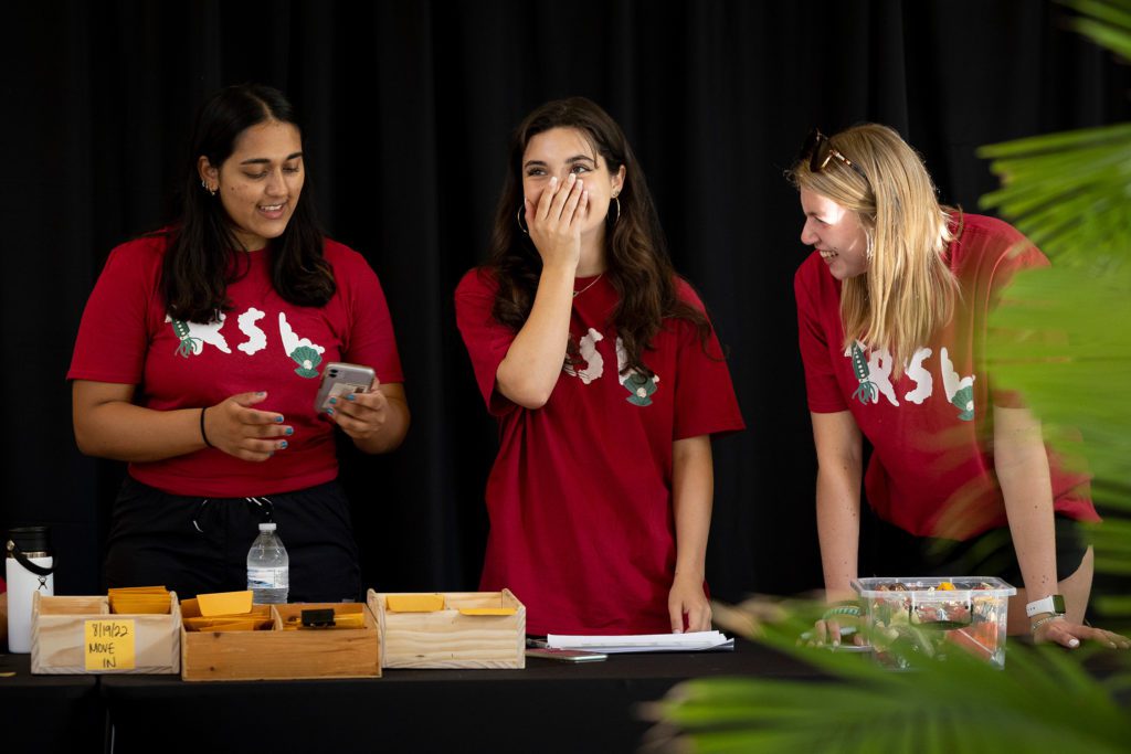 Three RSLs in their red t-shirts stand at a table at check-in.