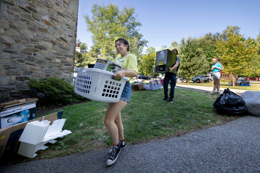 Three students on the Customs team move stuff into the dorms, including a full laundry basket and a minifridge