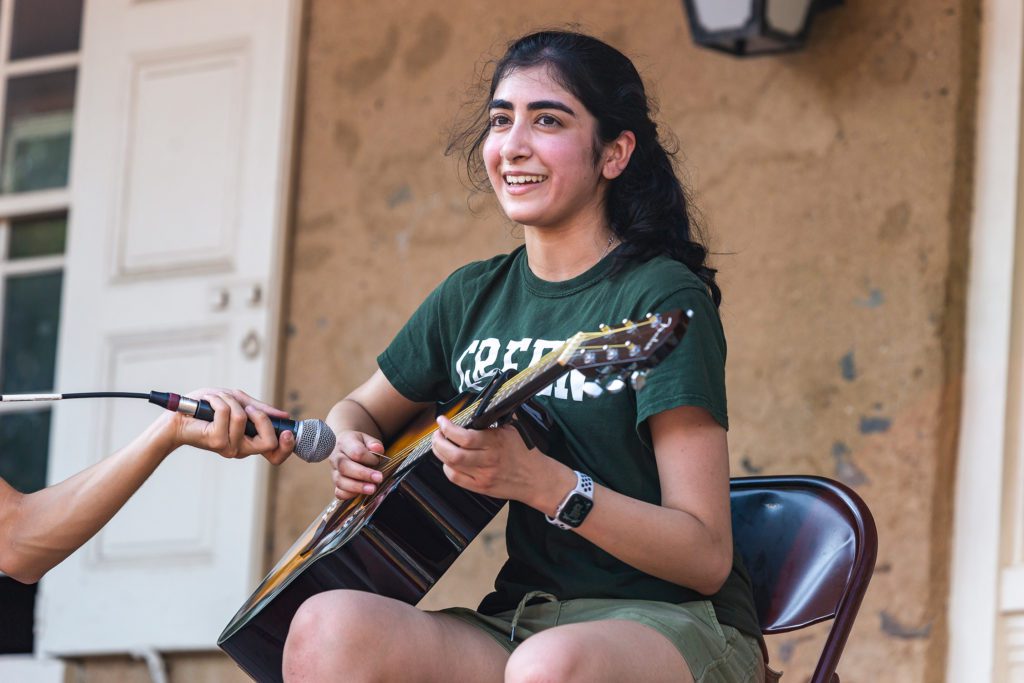 A student from the green team plays the guitar while an unseen person holds a microphone for them.