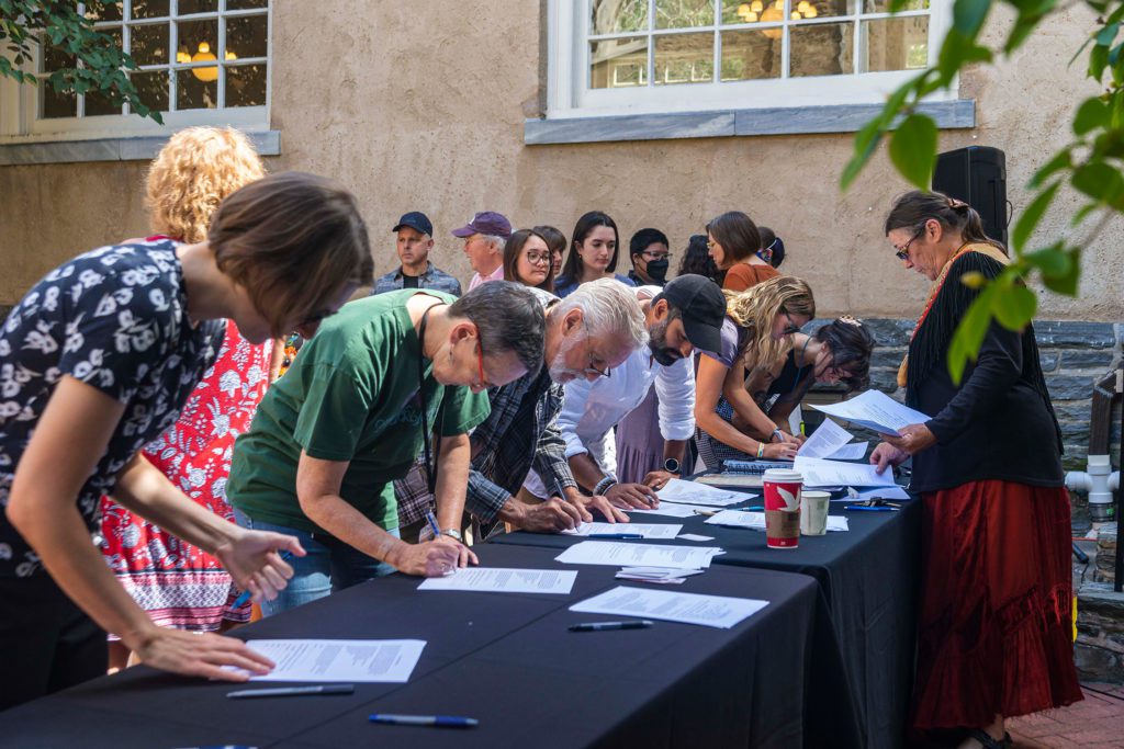 Seven people sign the treaty while Shelley DePaul looks on and several others wait for their turn to sign.