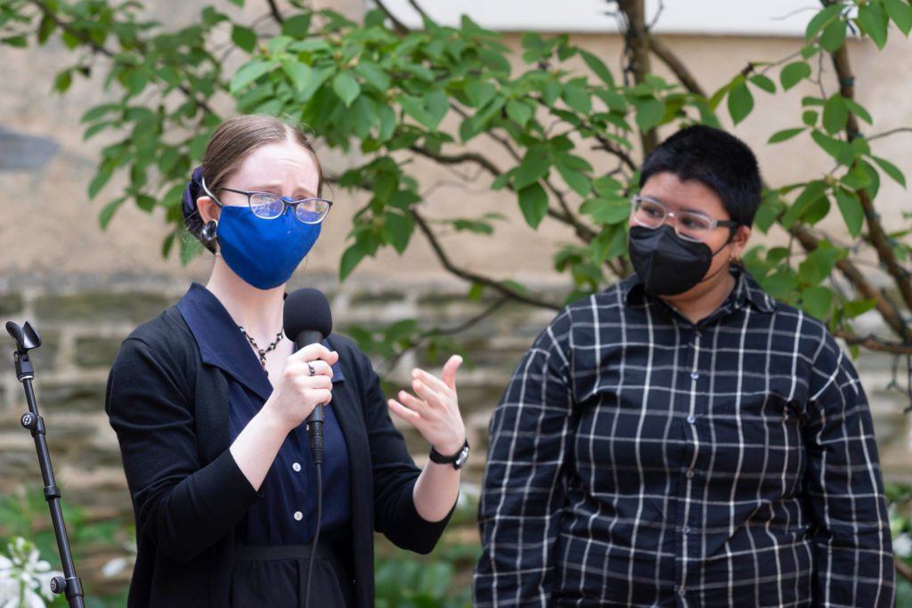 Lily Sweeney holds a microphone and Alex stands behind her.