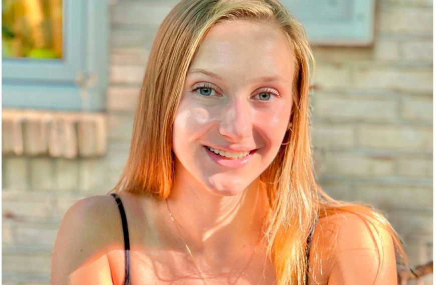 A headshot of Julie smiling outside a brick wall with the sunlight reflecting on her face.
