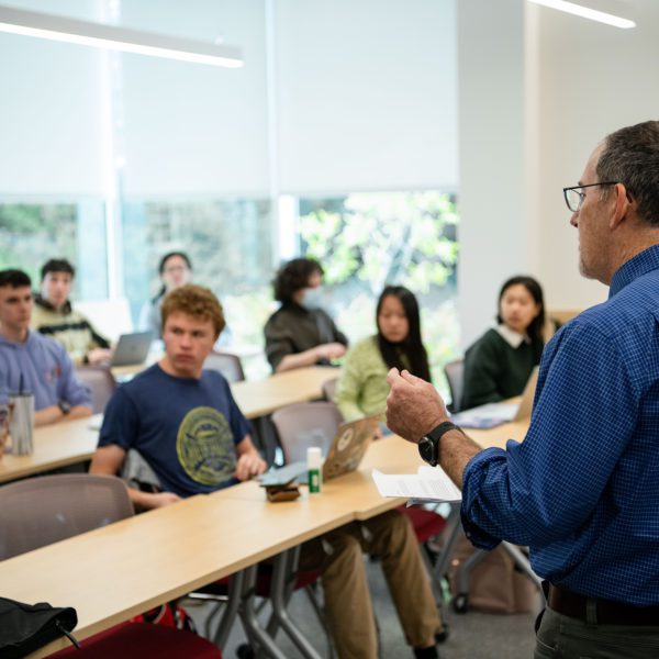 Richard Freedman stands at the front of class in. front of two rows of students seated at laptops.