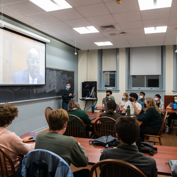Students sit around tables in a seminar room and the judge's large face appears onscreen in front of them.