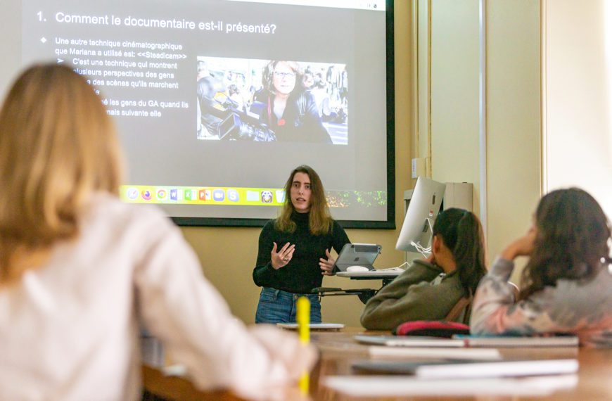 Kate stands in front of the class under a projection that reads "Comment le documentaire est-il présenté?"