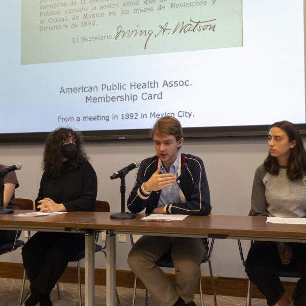 Four students sit at a table with a projection screen behind them.