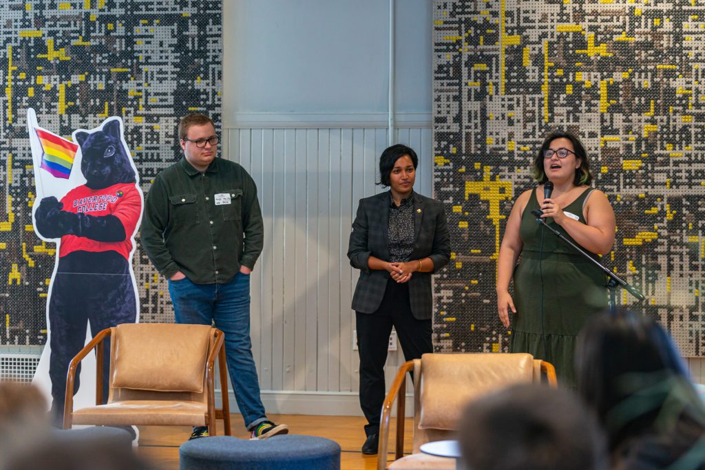 The three people stand next to a life-sized cutout of a black squirrel with a rainbow flag.