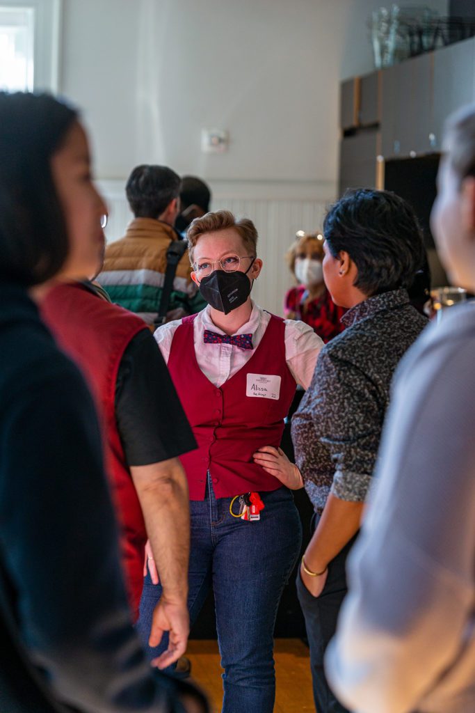 A student in a mask and bowtie stands in a crowd in the VCAM lobby.
