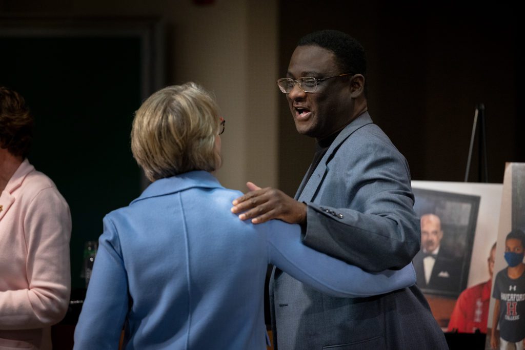 Rel and Wendy embrace with a portrait of Ira Reid visible in the background.