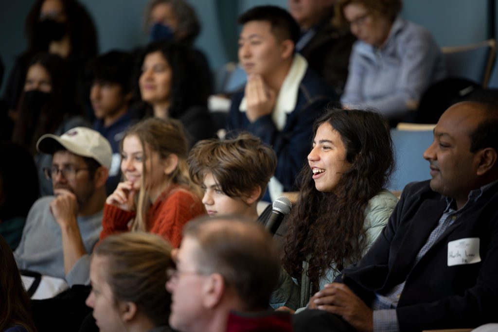 A group of students and family members laugh in their seats.