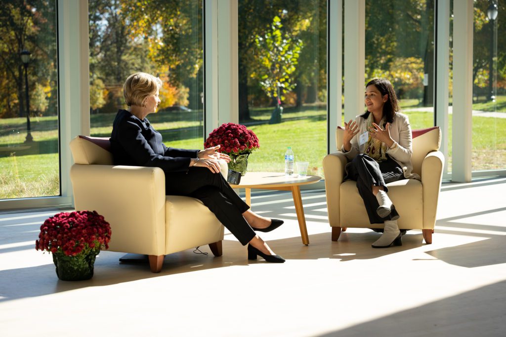 President Raymond and Professor Shirazi speak animatedly while bathed in light from the windows behind them.