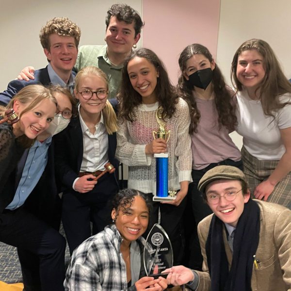 10 students huddled together posing with two trophies