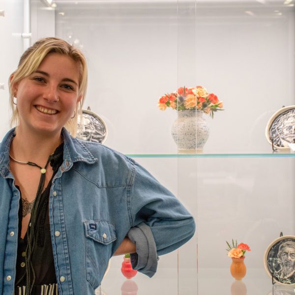 A photo of Edna in a blue shirt in front of her work in the VCAM 201 display case